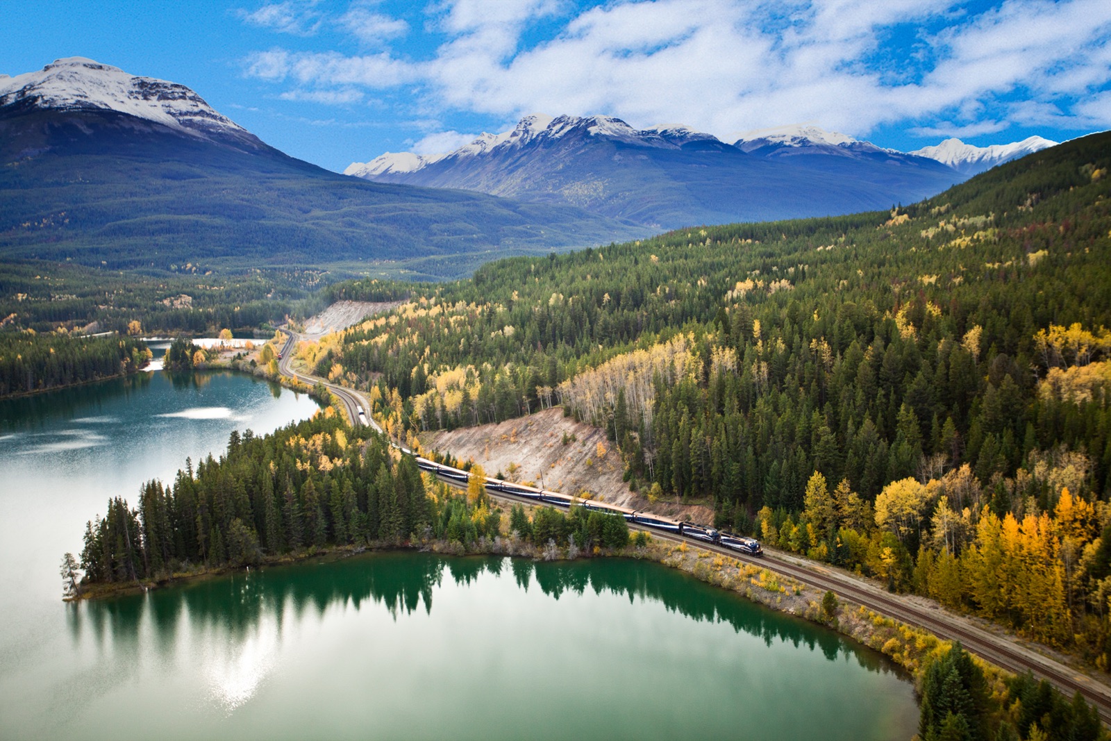 Rocky Mountaineer train winding past a turquoise lake and autumn forest in the Canadian Rockies