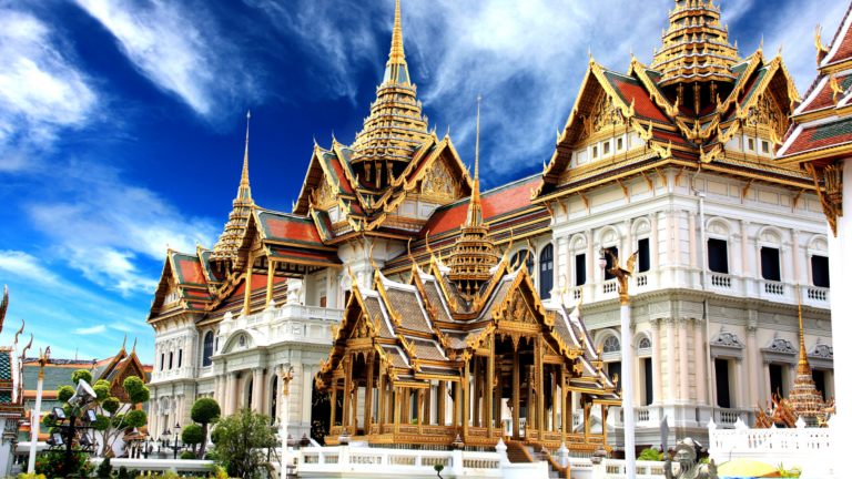 Golden Thai temple complex with ornate, gilded roofs and spires against a bright blue sky.