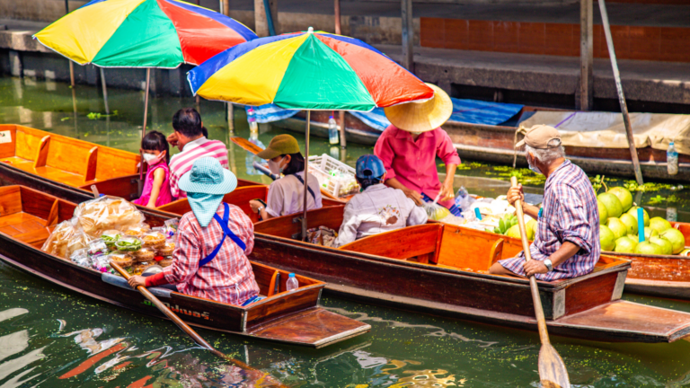 People in wooden boats selling fruit under colorful umbrellas on a canal.