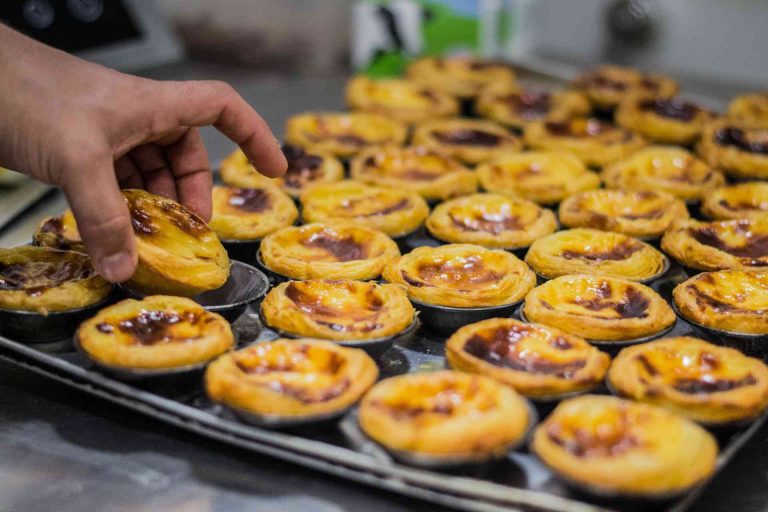 Hand picking a Portuguese custard tart from a tray of many in a bakery