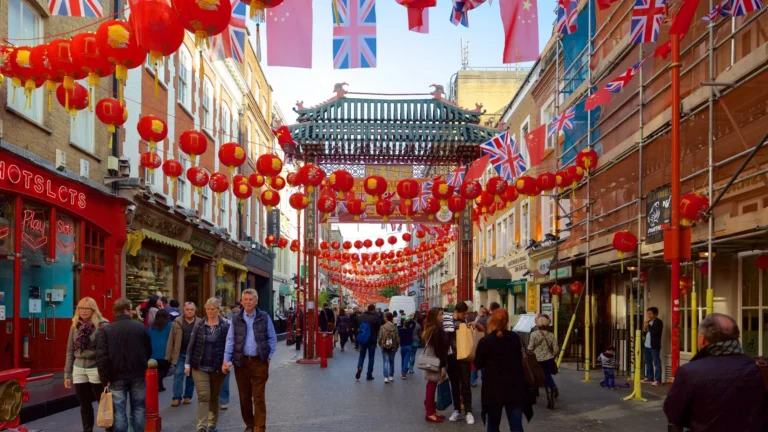Busy Chinatown street decorated with red lanterns and fluttering flags, including Union Jack and Chinese banners, with a green tiled gate in the distance.