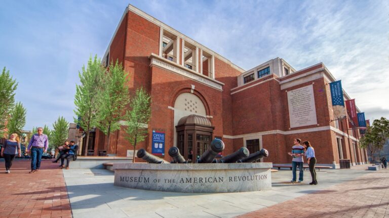 Brick Museum of the American Revolution building with cannons in the foreground and visitors walking outside on a sunny day.