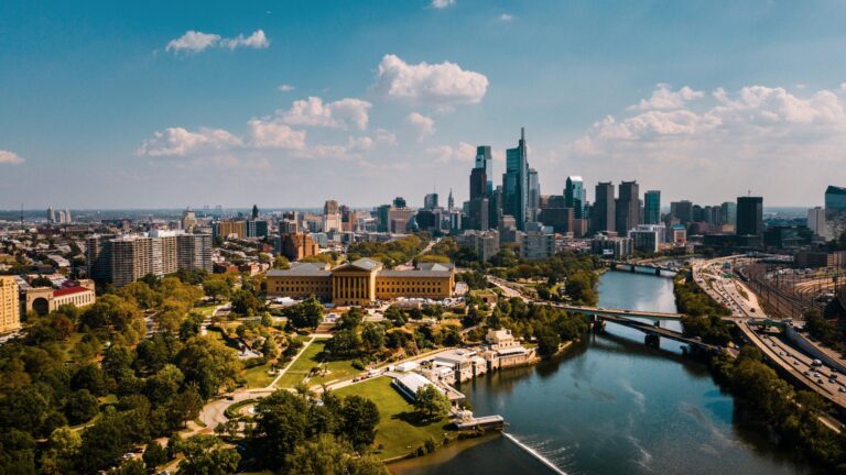 Aerial view of a downtown skyline with river, bridges, and green parks in foreground.